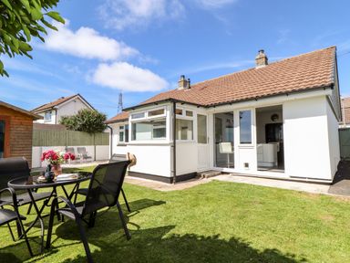 A backyard with a glass table and four chairs on a lawn next to a white house with a tiled roof at Summerhayes in Park Bottom
