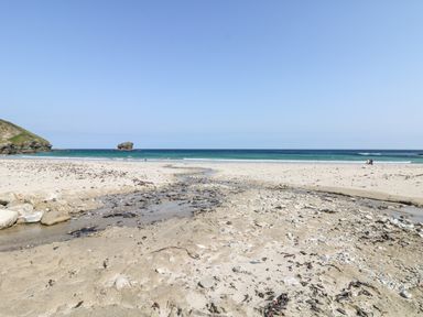 A sandy beach with a small stream flowing to the sea and a rock formation in the water at Summerhayes in Park Bottom