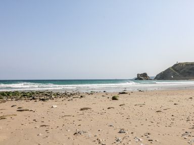 A sandy beach with scattered rocks and seaweed near the ocean with waves and cliffs in the background at Summerhayes in Park Bottom