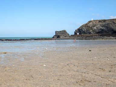 A beach with wet sand and two people walking near rocky cliffs and sea at Summerhayes in Park Bottom