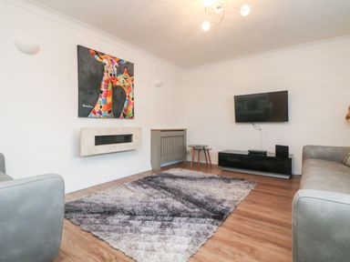 A living room with two gray sofas a colorful giraffe painting a wall mounted TV and a patterned rug at Summerhayes in Park Bottom