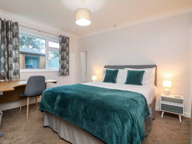 A bedroom with a double bed green blanket bedside table with lamp window desk and chair at Summerhayes in Park Bottom