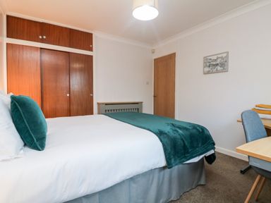 A bedroom with a bed green pillows green blanket wood built in wardrobe desk chair and folded towels on the desk at Summerhayes Park Bottom
