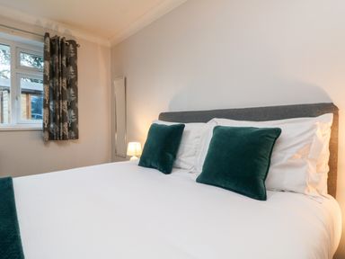 A bedroom with a bed with white sheets and green pillows next to a window with patterned curtains at Summerhayes in Park Bottom