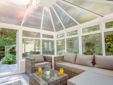 A conservatory with wicker furniture including a sofa and chair a glass table with two glasses of orange juice and a potted plant at Nant Cottage in Rowen