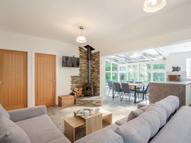 A living room with a gray sofa a wood stove and a dining area in a glass sunroom at Nant Cottage in Rowen