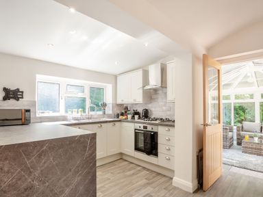 A kitchen with white cabinets and a marble countertop next to a conservatory with wicker furniture at Nant Cottage in Rowen