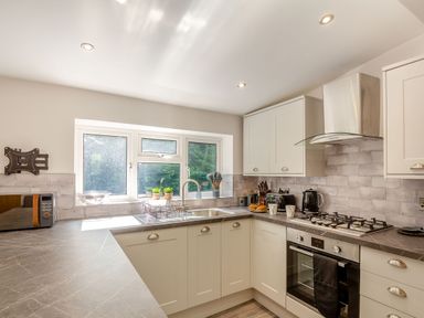 A kitchen with white cabinets gray countertops a stove oven microwave kettle and window at Nant Cottage in Rowen