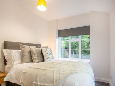 A bedroom with a bed with several pillows and a blanket near a window with a dark roller blind at Nant Cottage in Rowen