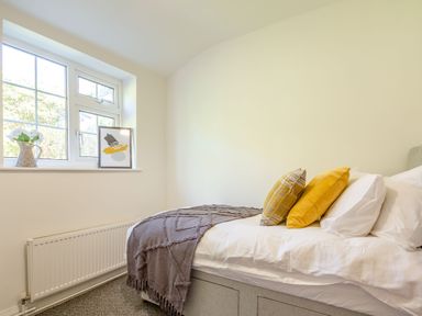 A bedroom with a bed with pillows and a throw beside a window with a flower vase and artwork at Nant Cottage in Rowen