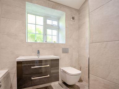 A bathroom with a wall-mounted toilet and a sink with a cabinet under a window at Nant Cottage in Rowen