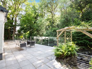An outdoor patio area with chairs and a table next to trees and a wooden garden arch at Nant Cottage in Rowen