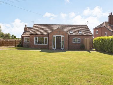 A brick house with a tiled roof and green lawn in front at The Croft in Thompson near Watton