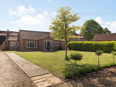 A brick house with a tiled roof a lawn with trees and a paved pathway at The Croft in Thompson near Watton