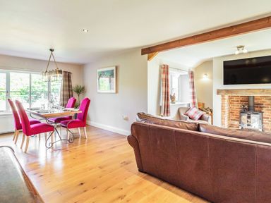 A dining area with pink chairs and a wooden table next to a living room with a brown sofa and a fireplace at The Croft Thompson near Watton