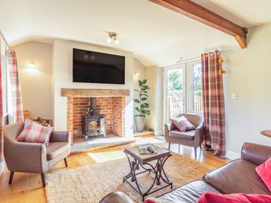 A sitting room with a wood stove fireplace two armchairs a sofa a coffee table and a television at The Croft in Thompson near Watton