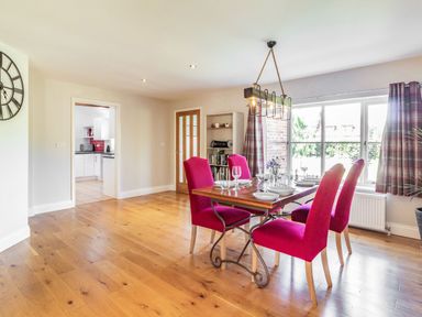 A dining room with a table and four red chairs near a window and a doorway to a kitchen at The Croft in Thompson near Watton