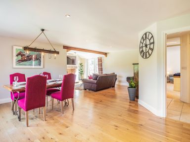 A dining area with a wooden table and six red chairs next to a living room with brown sofas and a wall clock at The Croft in Thompson near Watton