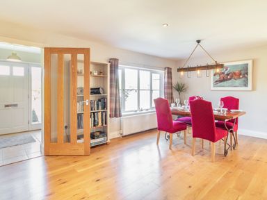 A dining room with a wooden table and four red chairs near a window and a bookshelf at The Croft in Thompson near Watton