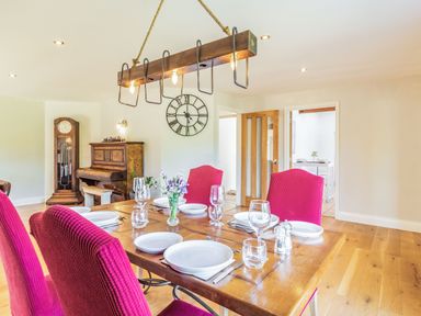 A dining room with a wooden table set for six with flowers in a vase and magenta chairs at The Croft in Thompson near Watton