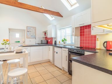 A kitchen with white cabinets red tiled backsplash and a small dining table with stools at The Croft in Thompson near Watton