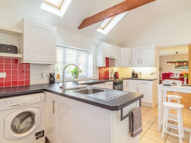 A kitchen with white cabinets black countertops a washing machine and a small dining table with stools at The Croft in Thompson near Watton