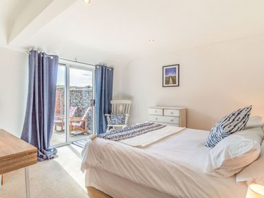 A bedroom with a bed a desk a white dresser a chair and sliding glass doors with blue curtains at The Croft in Thompson near Watton