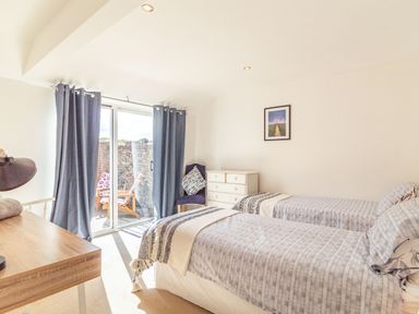 A bedroom with two single beds a dresser a desk and sliding glass doors with curtains at The Croft in Thompson near Watton