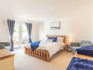 A bedroom with a wooden bed blue cushions and curtains two armchairs and towels on a dresser at The Croft in Thompson near Watton