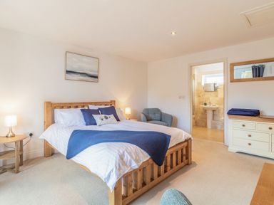 A bedroom with a wooden double bed bedside tables a blue armchair and an en suite bathroom at The Croft in Thompson near Watton