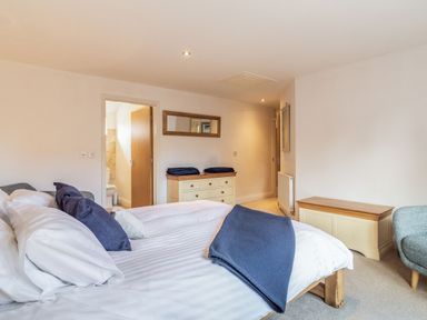 A bedroom with a made bed with blue pillows and blankets a dresser with folded blankets a mirror an armchair and a chest at The Croft in Thompson near Watton