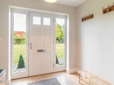 A hallway with a white front door flanked by glass panels wooden coat racks and a wooden shoe rack at The Croft in Thompson near Watton