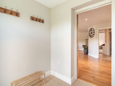 A hallway with wooden coat hooks and a shoe rack next to a doorway leading to a room with wooden flooring at The Croft in Thompson near Watton