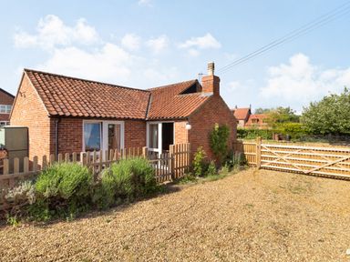A brick house with a tiled roof gravel driveway and wooden fence at The Croft in Thompson near Watton