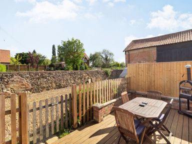 An outdoor wooden deck with table and chairs next to a fenced garden area at The Croft in Thompson near Watton