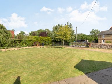 A garden with a lawn trees hedges and a gate leading to a driveway at The Croft in Thompson near Watton