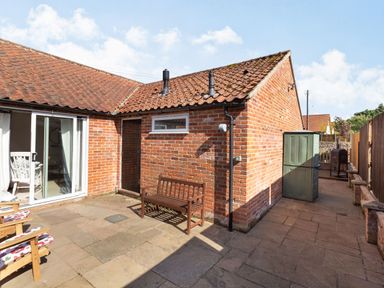 A paved outdoor patio area with wooden bench and chairs next to a brick building at The Croft in Thompson near Watton