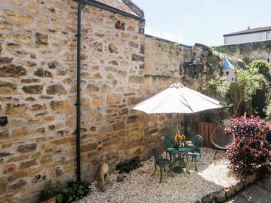 A small outdoor patio with a metal table and chairs under a white umbrella next to a stone wall at Beals Yard in Alnwick