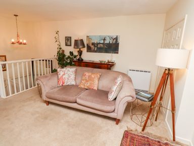 A sitting area with a sofa, cushions, a floor lamp, side table with books, a wooden sideboard with a lamp and plants at Beals Yard in Alnwick