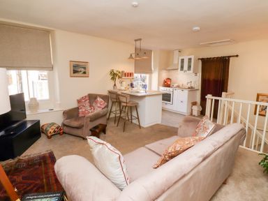 A living room with beige sofas and armchair next to a kitchen island with bar stools at Beals Yard in Alnwick