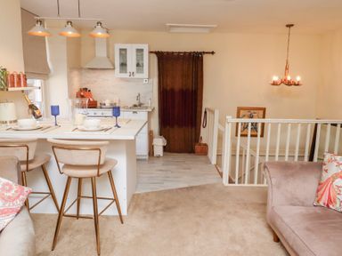 A kitchen and dining area with bar stools plates glasses and a couch with pillows at Beals Yard in Alnwick