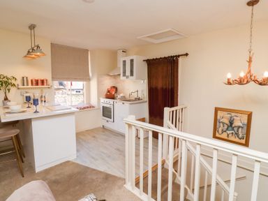 A kitchen with white cabinets a window with a blind and a countertop with blue glasses and bowls at Beals Yard in Alnwick