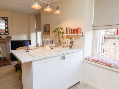 A dining area with a white kitchen island set with blue glasses and plates at Beals Yard in Alnwick