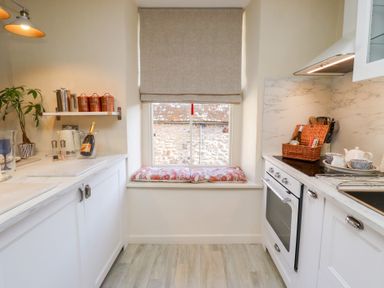 A kitchen with white cabinets a window with a cushion and cooking utensils at Beals Yard in Alnwick