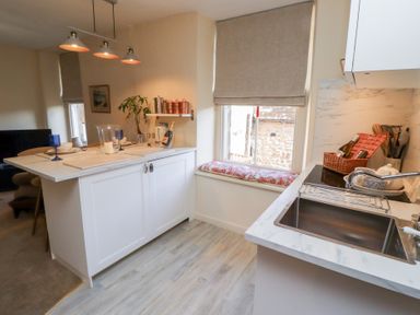 A kitchen with white cabinets a sink a window with a cushion and an island counter at Beals Yard in Alnwick