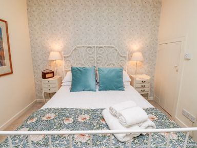 A bedroom with a white metal bed frame with white bed linens and teal pillows two bedside tables with lamps and a floral patterned blanket at Beals Yard in Alnwick