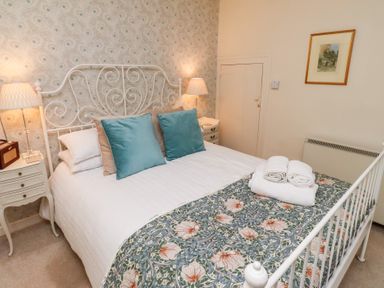 A bedroom with a double bed with pillows and towels bedside tables with lamps wallpaper and framed picture at Beals Yard in Alnwick