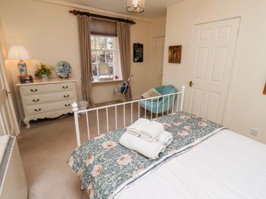 A bedroom with a bed folded towels on dresser window with curtains chair and chest of drawers at Beals Yard Alnwick