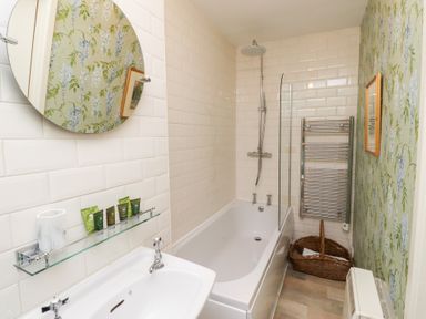 A bathroom with a bathtub a shower a sink a round mirror and floral wallpaper at Beals Yard in Alnwick