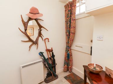 A hallway with a white door a coat stand with walking sticks a mirror with antler frame and a wooden table at Beals Yard Alnwick